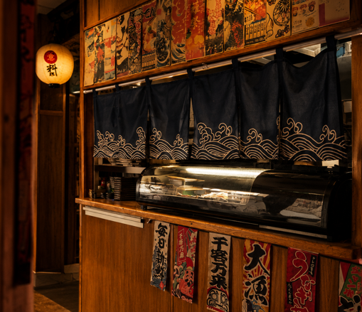 Sushi counter with noren curtains and lantern at Izushi Izakaya